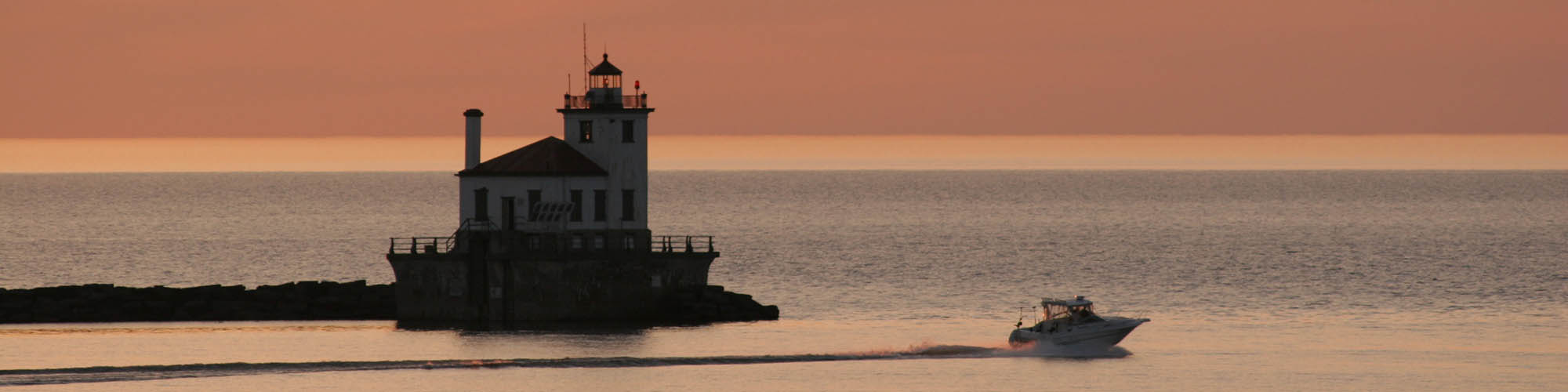 motor boat in Oswego Harbor moving past the lighthouse at sunset